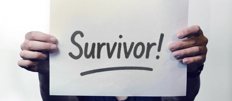 A person holding up a sign that says Survivor!
